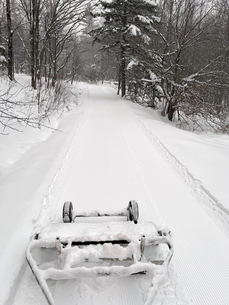 Groomed snow trail with fresh corduroy behind a tow-behind groomer