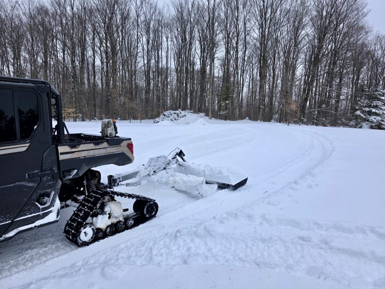 Tow-behind trail groomer behind a tracked UTV on a groomed trail